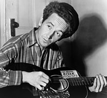 Woody Guthrie with guitar labeled  This Machine Kills Fascists